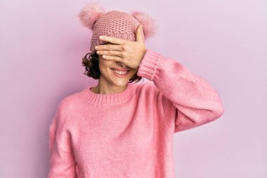 Şirin yün şapka takan esmer bir kadın. Gülümsüyor ve elleri yüzünde, şaşırmak için gözlerini kapatıyor. kör kavram. 