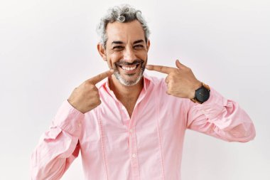 Orta yaşlı, ispanyol bir adam izole edilmiş arka planda gülümsüyor ve parmaklarıyla ve ağzıyla işaret ediyor. diş sağlığı kavramı. 