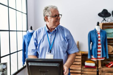 Orta yaşlı, gri saçlı, gülümseyen, kendine güvenen bir adam giyim mağazasında çalışıyor.