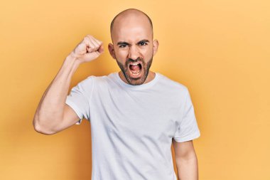 Genç, kel bir adam, kızgın ve kızgın. Öfkeyle bağırırken yumruğunu kaldırıyor. öfke ve agresif konsept. 