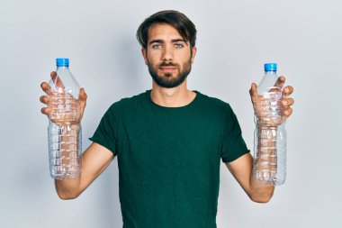 Elinde geri dönüşüm şişeleri tutan İspanyol genç adam yüzünde ciddi bir ifadeyle rahatladı. Basit ve doğal bir şekilde kameraya bakıyorsun.. 