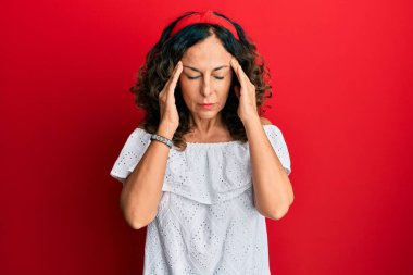 Orta yaşlı İspanyol kadın stres yüzünden elleri başının üstünde gündelik kıyafetler giyiyor. migren ağrısı. 