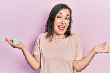 Orta yaşlı İspanyol kadın elinde kozmetik nemlendirici yüz kremi tutarak başarıyı mutlu bir gülümsemeyle ve kazanan yüz ifadesiyle kutluyor. 