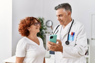 Orta yaşlı erkek ve kadın doktor üniforması giyiyor. Akıllı telefon kullanıyor. Klinikte tıbbi danışmanlık yapıyorlar.