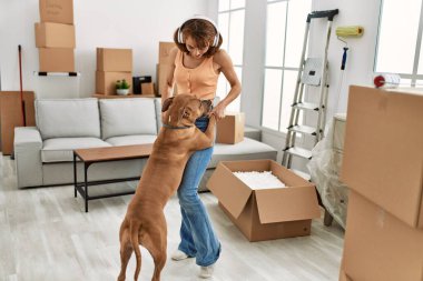 Beyaz bir kadın, kendinden emin bir şekilde gülümsüyor müzik dinliyor ve evde köpekle dans ediyor.