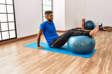 Yakışıklı İspanyol adam egzersiz yapıyor ve yoga minderinde geriniyor, spor salonunda pilates topuyla esneklik gösteriyor.