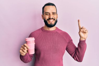 Sakallı genç bir adam bir fincan kahve içerken bir fikir veya soru işareti ile gülümsüyor mutlu bir yüzle, bir numara 