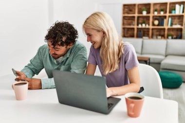 Laptop ve akıllı telefon kullanan genç bir çift evde kahve içiyor..