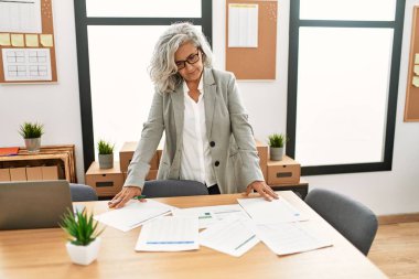 Ofiste çalışan orta yaşlı, kır saçlı bir iş kadını..