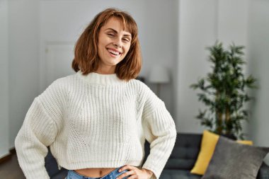 Genç, beyaz bir kadın gülümseyerek evde dikiliyor.