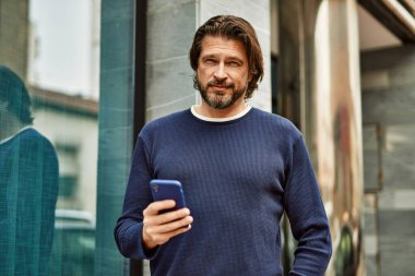 Kasabada akıllı telefon kullanan orta yaşlı yakışıklı bir adam.