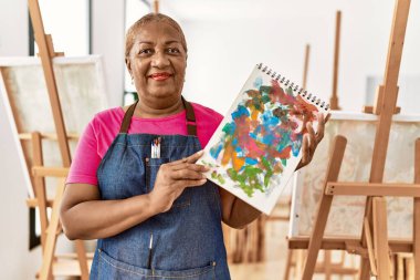 Kıdemli Afro-Amerikan kadın gülümsüyor sanat stüdyosunda kendine güvenen çizim defteri tutuyor.