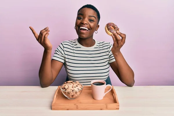 Młoda Afroamerykanka Jedząca Śniadanie Trzymając Czekoladowego Pączka Uśmiechając Się Szczęśliwa — Zdjęcie stockowe