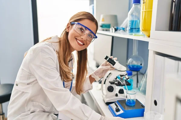 实验室显微镜下身穿科学家制服的金发年轻女子 — 图库照片