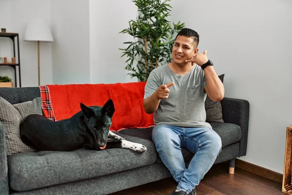 Jovem Latino Cão Sentado Sofá Casa Sorrindo Fazendo Falar Gesto — Fotografia de Stock