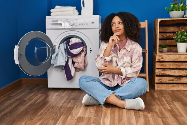 若いアフリカ系アメリカ人の女性が洗濯をしている床の上に座っている深刻な顔あごに手で質問について考え 混乱のアイデアについて思慮深く — ストック写真