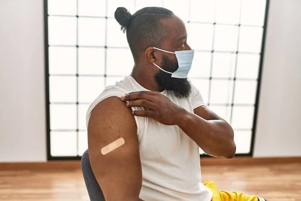 若いアフリカ系アメリカ人男性は クリニックでのCovid 19ワクチン接種のためのバンド援助を示しています — ストック写真
