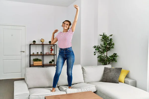 Young woman listening to music and dancing standing on sofa at home