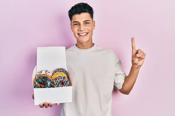 Joven Hombre Hispano Sosteniendo Caja Sabrosas Rosquillas Coloridas Sonriendo Con —  Fotos de Stock
