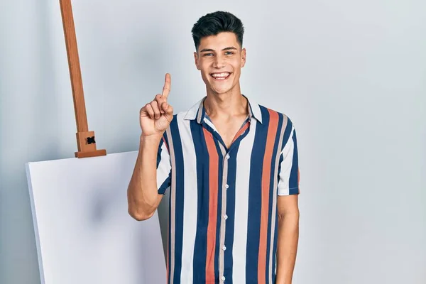 Νεαρός Ισπανός Στέκεται Κοντά Άδειο Καμβά Δείχνοντας Και Δείχνοντας Δάχτυλο — Φωτογραφία Αρχείου