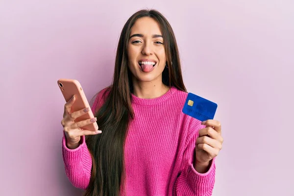 Młoda Latynoska Dziewczyna Trzyma Smartfona Kartę Kredytową Wystający Język Szczęśliwy — Zdjęcie stockowe