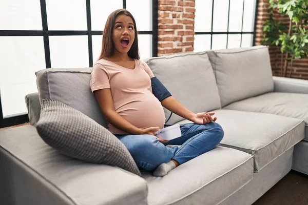 若いです妊娠中の女性血圧モニターを使用してソファの上に座って怒っていると怒っている叫びフラストレーションと激怒 怒りで叫んで検索 — ストック写真