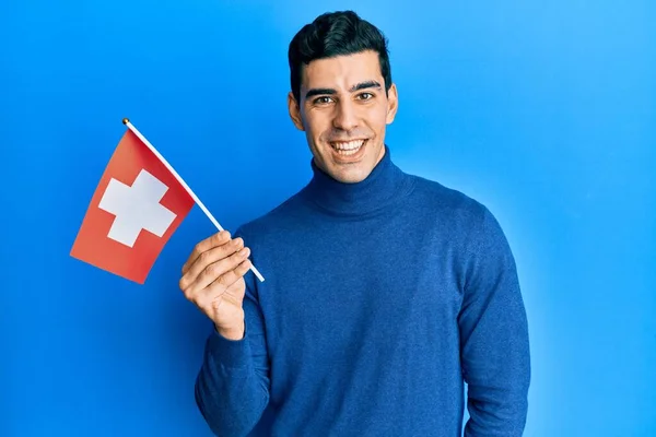 Snygg Hispanic Man Håller Switzerland Flagga Ser Positiv Och Glad — Stockfoto