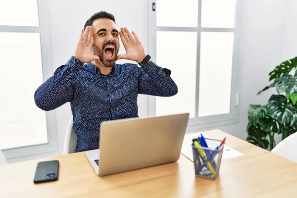髭を生やした若いヒスパニック系の男がオフィスで働いていて ノートパソコンは陽気に手を顔を見せて竹を覗かせて笑っていた びっくりして興奮しました — ストック写真