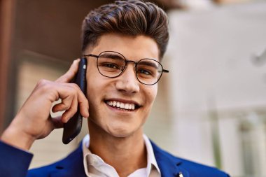 Akıllı telefondan konuşan genç adam sokakta takım elbise ve gözlük takıyor.