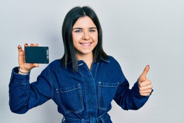 Genç esmer kadın mutlu ve pozitif gülümsüyor, başparmağıyla mükemmel ve onay işareti yapıyor. 