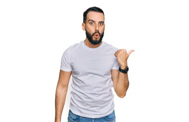 Sakallı, sıradan beyaz tişörtlü genç bir adam elleri yana dönük, ağzı açık, şaşkın bir ifadeyle şaşırdı.. 