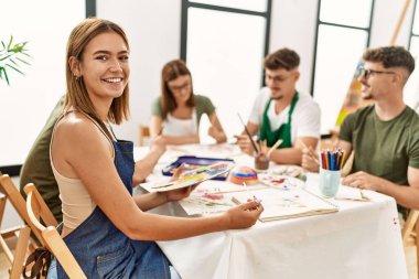 Sanat stüdyosundaki bir grup insanla mutlu bir resim çizen genç bir kadın..