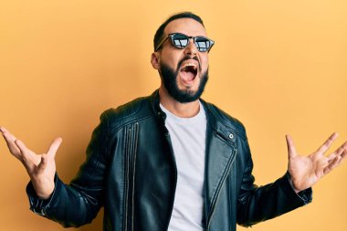 Siyah deri ceketli, güneş gözlüklü, deli gibi bağıran, sinirli ifadeli ve kollarını kaldırmış genç bir adam. hüsran kavramı. 