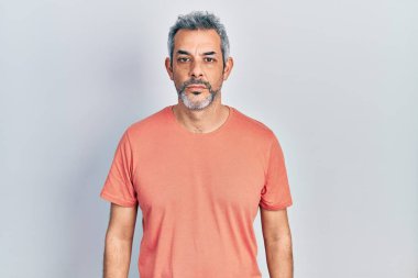 Gri saçlı, sıradan tişörtler giyen yakışıklı, orta yaşlı bir adam. Yüzünde ciddi bir ifadeyle rahatlamış. Basit ve doğal bir şekilde kameraya bakıyorsun.. 