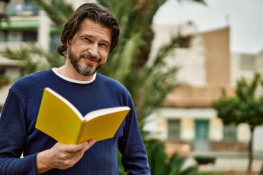 Orta yaşlı yakışıklı bir adam parkta kitap okuyor.