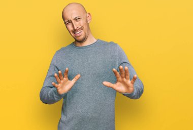 Kel, sakallı, sıradan kıyafetler giyen, tiksindirici bir yüz ifadesi takınan, tiksindirici, tiksindirici bir yüz ifadesi olan bir adam. Eller havada. 