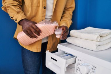 Genç Afrikalı Amerikalı adam gülümsüyor Çamaşır odasında çamaşır makinesine deterjan döküyor