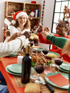 Bir grup genç, mutlu bir şekilde gülümseyerek evde Noel yemeği yiyor..