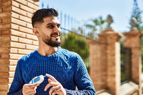 Young arab man smiling confident holding glucometer at street