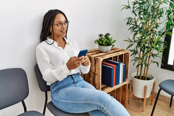 Genç Afrikalı Amerikalı Kadın Bekleme Odasında Akıllı Telefon Kullanarak Gülümsüyor — Stok fotoğraf
