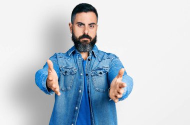 Sakallı, kolları açık İspanyol bir adam sarılma hareketi yapıyor. Yüzünde ciddi bir ifade var. Basit ve doğal bir şekilde kameraya bakıyorsun.. 