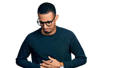 Genç Afro-Amerikalı bir adam günlük kıyafetler giyiyor ve elleri karnında gözlükler takıyor çünkü hazımsızlık, acı verici bir hastalık ve kendini iyi hissetmiyor. Ağrı kavramı. 