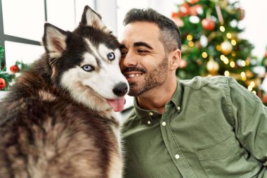 Evdeki Noel ağacının yanında köpekle kanepede otururken kendine güvenen İspanyol genç adam.