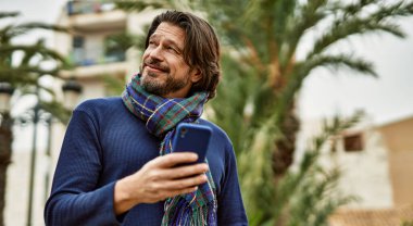 Parkta akıllı telefon kullanan orta yaşlı yakışıklı bir adam.