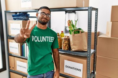 Genç Hintli gönüllü bağış kutusu tutuyor gülümsüyor ve parmaklarını zafer işareti yaparken kameraya bakıyor. İki numara.. 