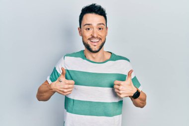 Gündelik kıyafetler giyen genç İspanyol adam. Başarı işareti yapıyor. Elleriyle olumlu jest yapıyor. Neşeli ifade ve kazanan jest. 