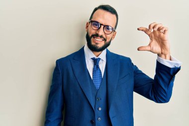 Sakallı, takım elbiseli, kravatlı, gülümseyen, kendine güvenen, el hareketi yapan, parmaklarıyla işaret eden ve kameraya bakan genç bir adam. ölçüm kavramı. 