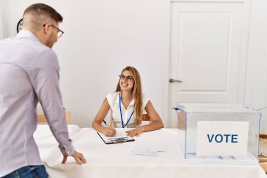 Genç seçmen seçim masasında duruyor ve seçim merkezinde siyasi parti işçisiyle konuşuyor..