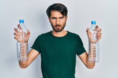 Plastik şişeleri geri dönüşüm için tutan genç İspanyol adam şüpheci ve gergin, sorun yüzünden surat asıyor. negatif kişi. 