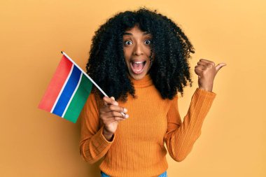 Afro saçlı, gambiya bayrağı taşıyan, ağzı açık gülümseyen Afro-Amerikalı bir kadın. 